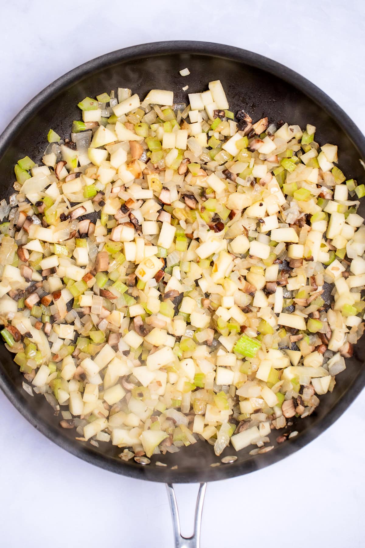 A saute pan with onion, celery, mushrooms, and apple pieces being cooked.