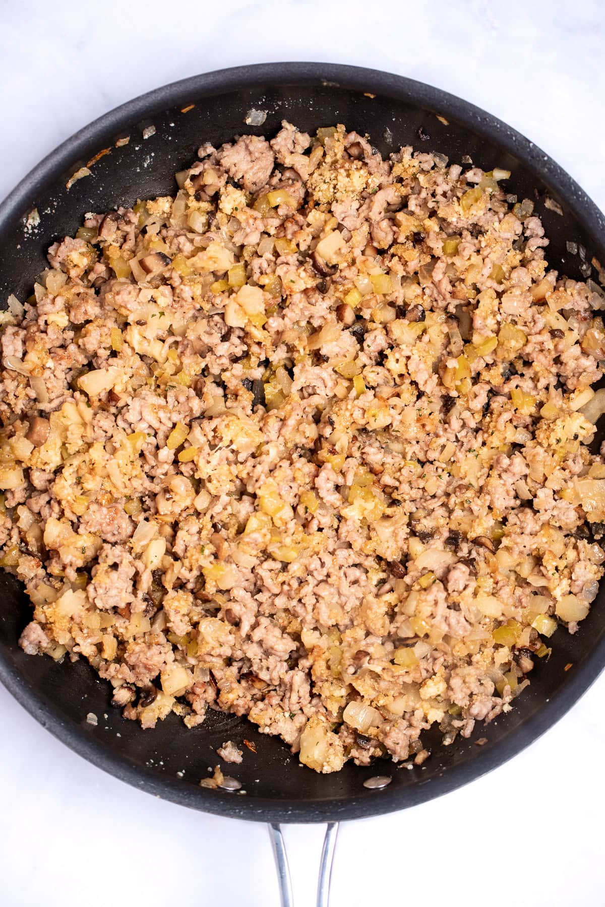 A saute pan with cooked ground sausage and vegetables mixed together.