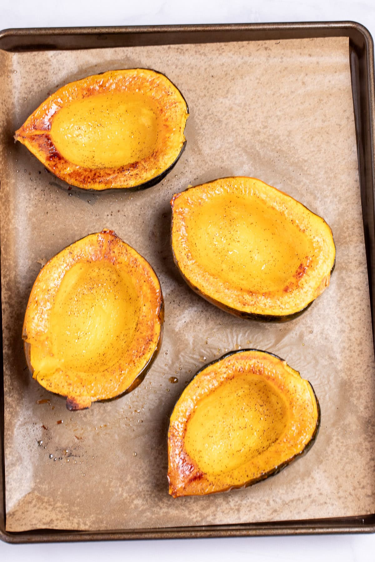 Four halves of acorn squash open-side-up after being roasted with olive oil and pepper.
