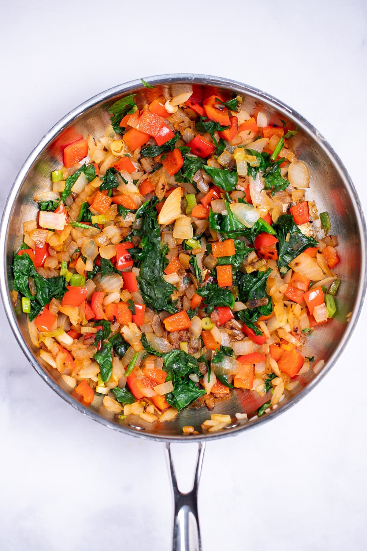 A skillet with onion, spinach, green onion, and bell pepper sautéed.