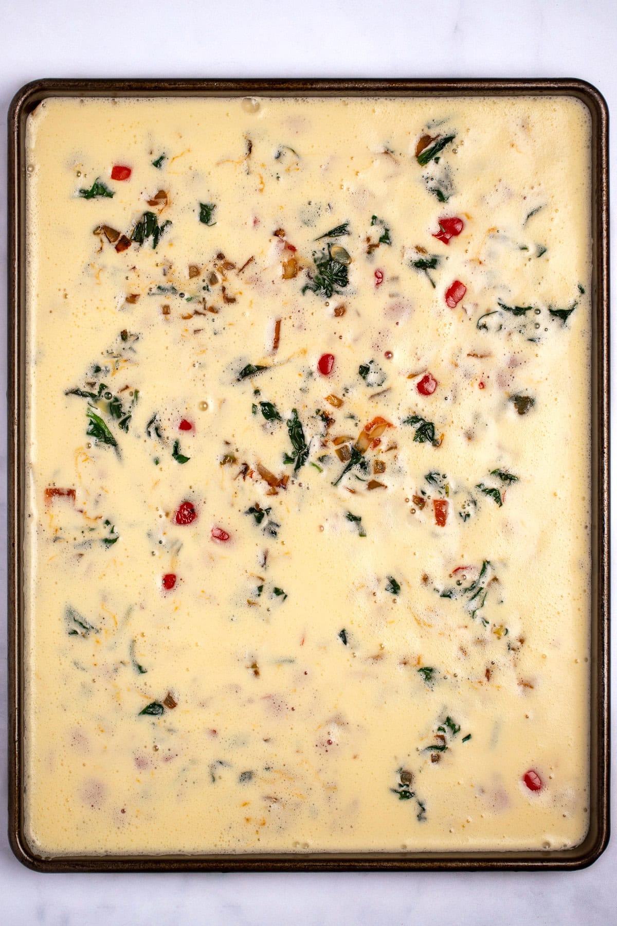 A sheet pan with a blended egg mixture and vegetables before being cooked.