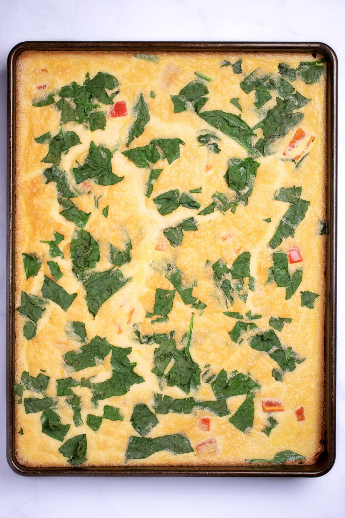 A sheet pan with fully cooked eggs with spinach and bell pepper.