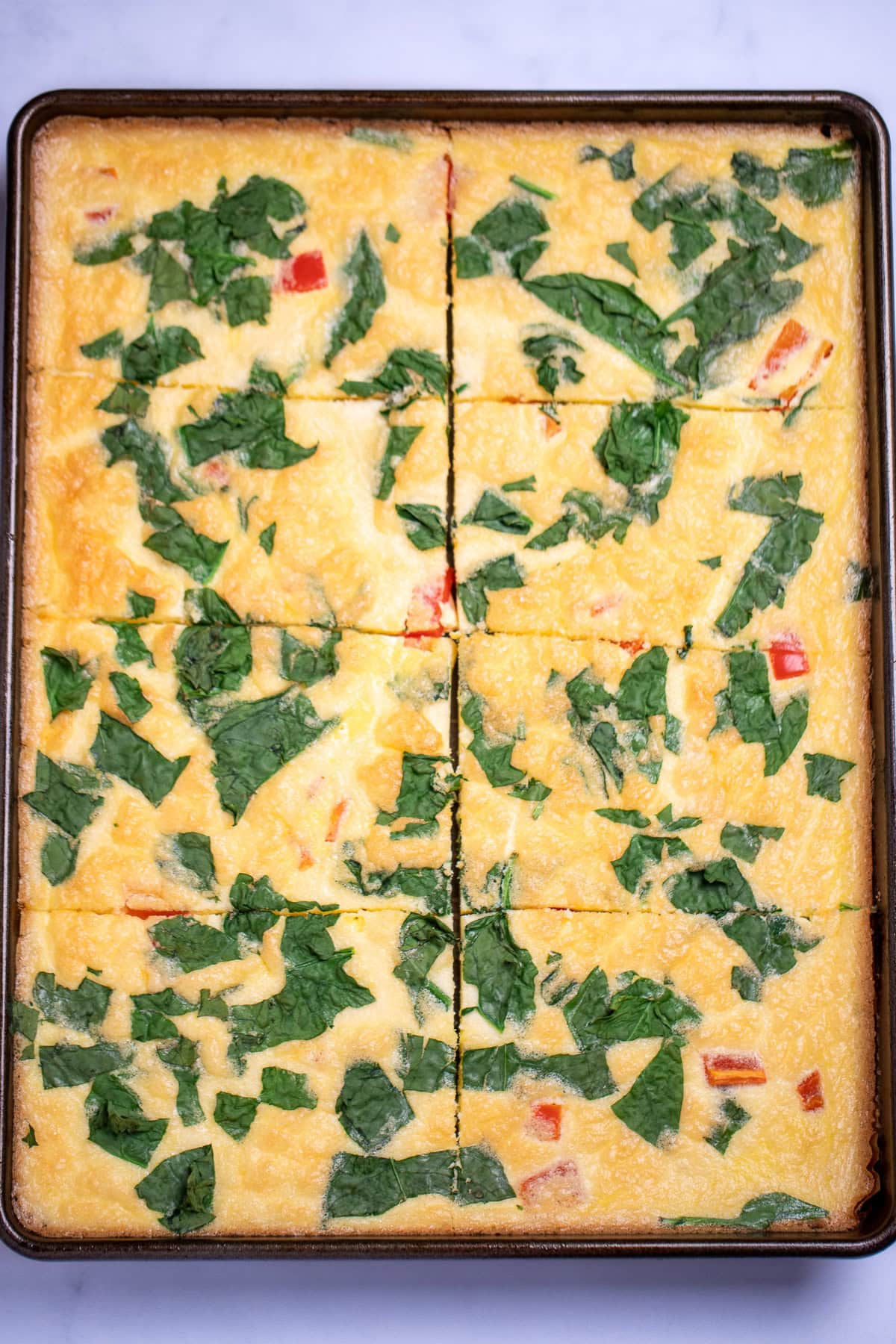 A sheet pan with fully cooked eggs with spinach and bell pepper, cut into 6 pieces.