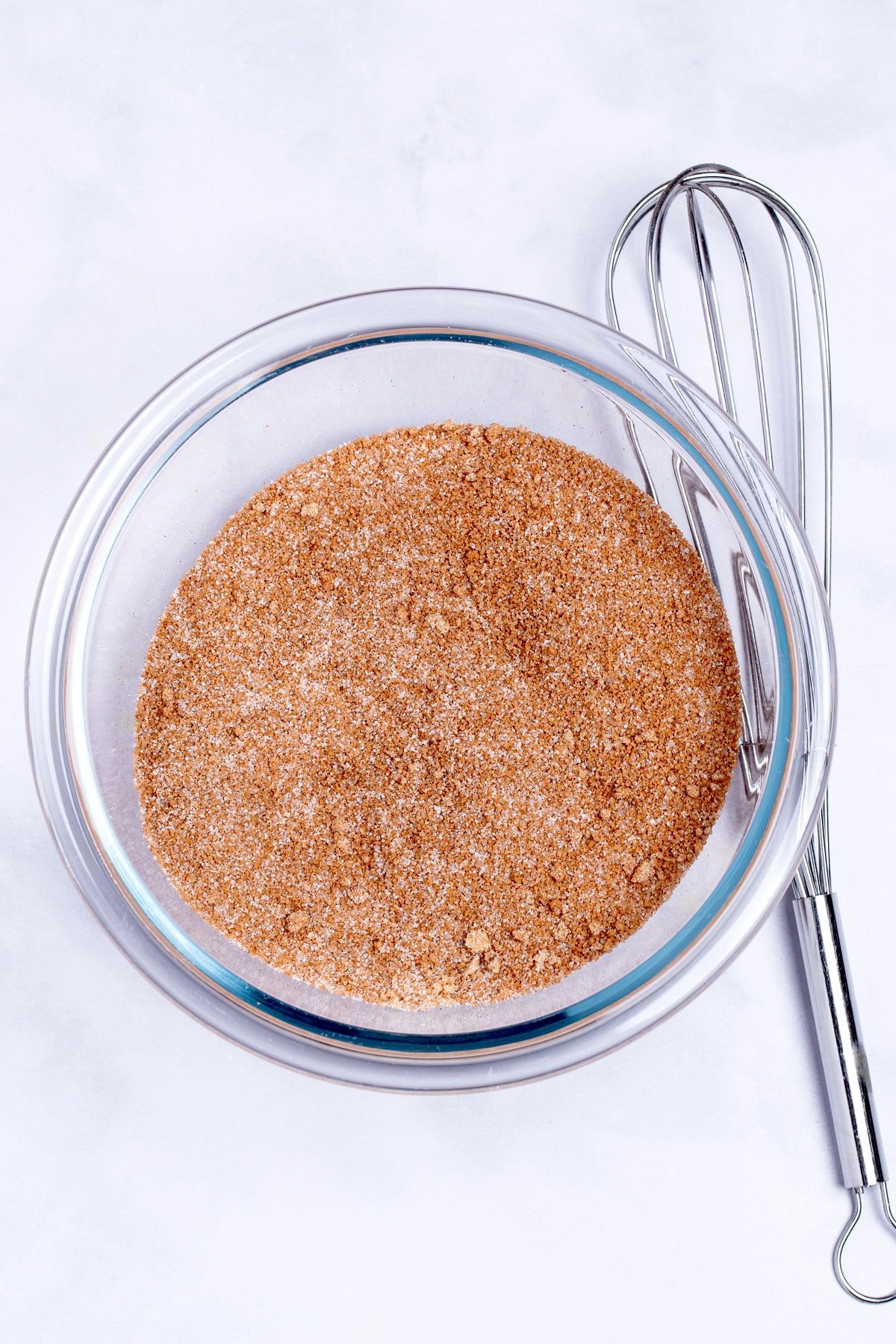 A glass bowl on a table with brown and granulated sugar whisked together.