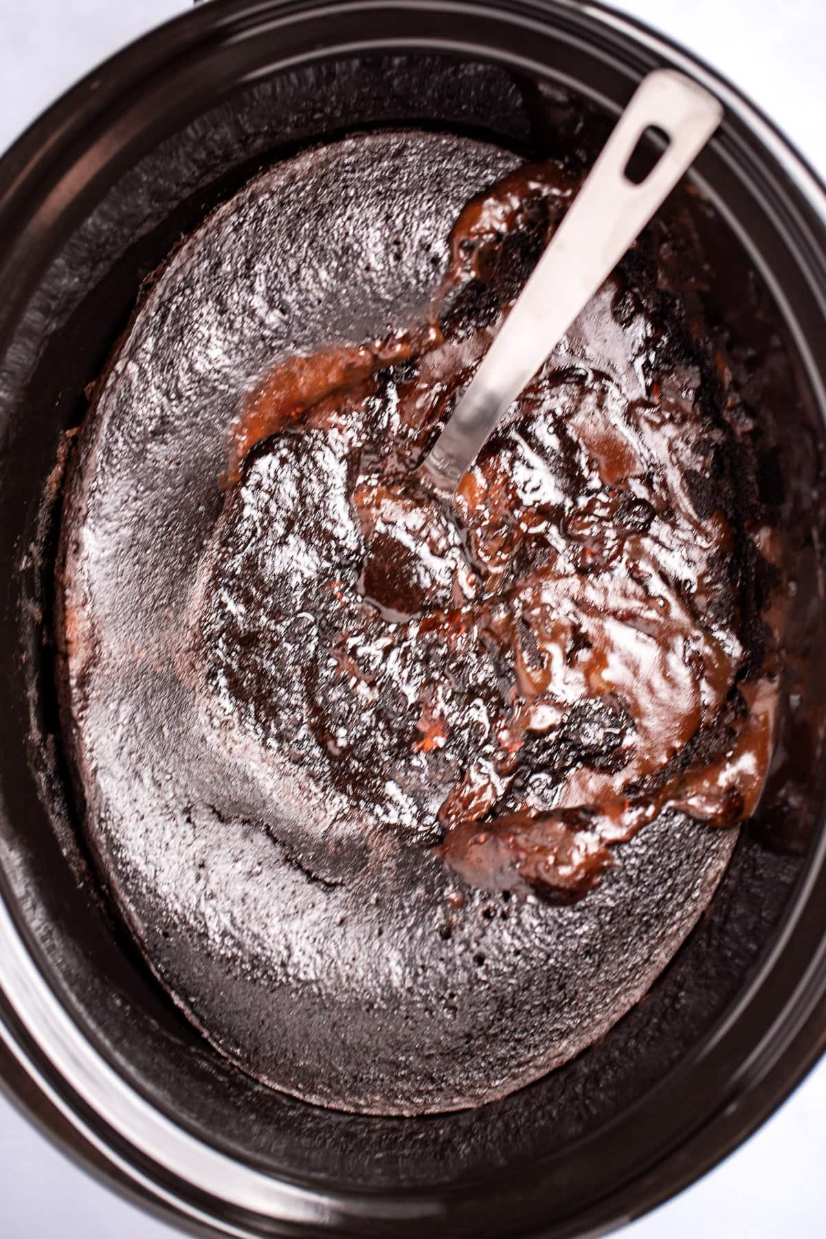 A slow cooker with chocolate lava cake, and a spoon in the cake.