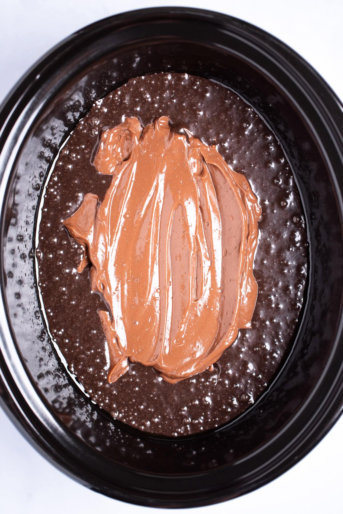 A slow cooker with chocolate cake batter topped with chocolate pudding before being cooked.