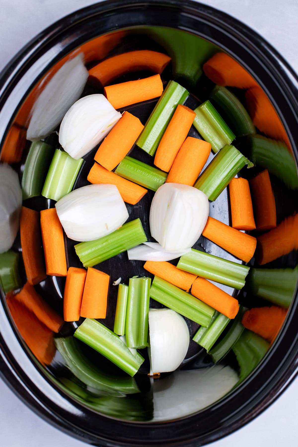A slow cooker with chopped celery, carrot, and onion in the bottom before being cooked.