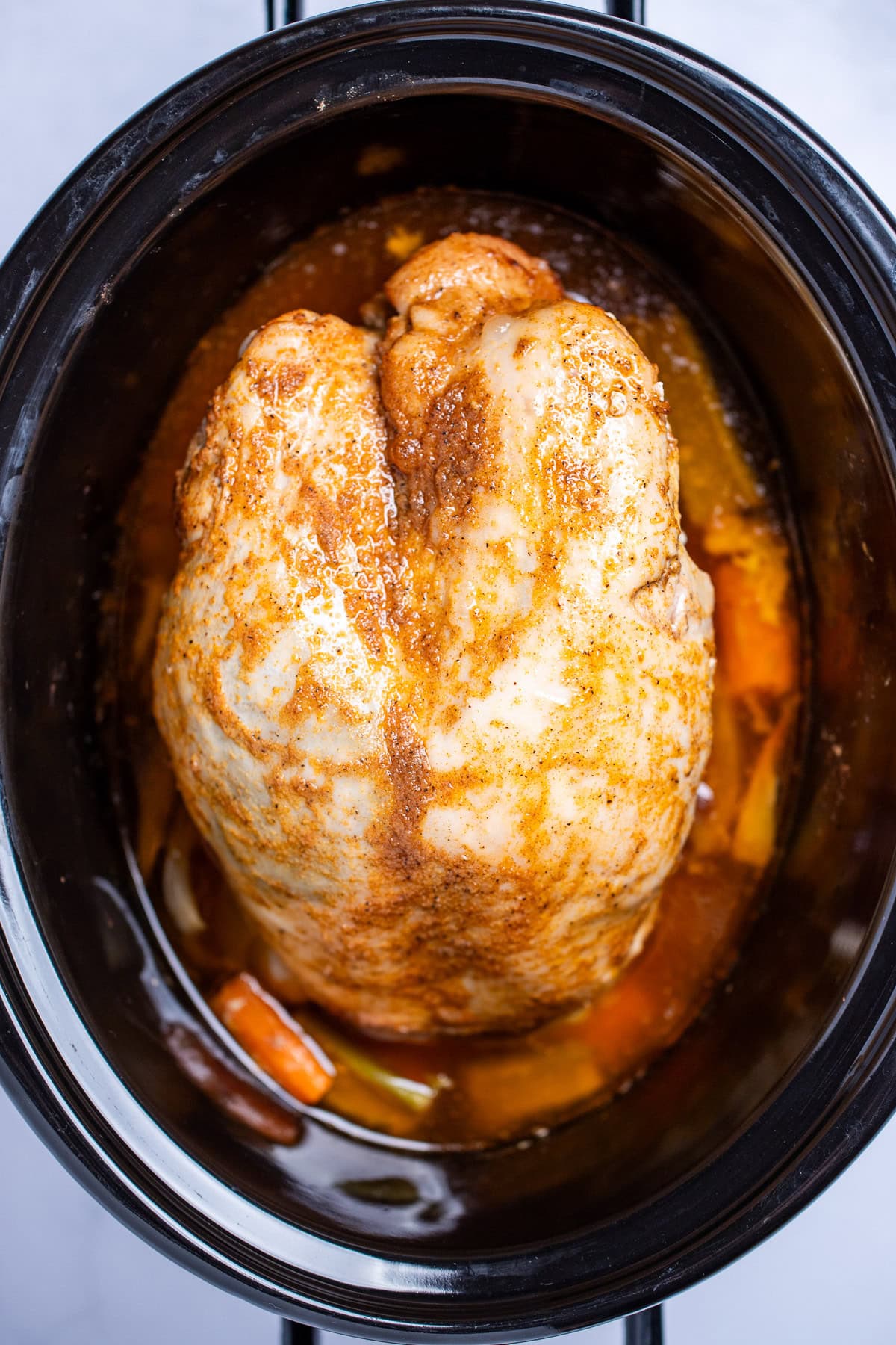 A slow cooker with a fully cooked turkey breast on top of vegetables and turkey drippings.