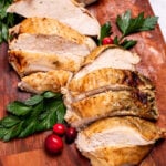A cutting board with sliced turkey breast next to parsley and cranberries.