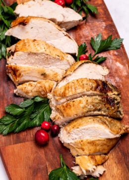 A cutting board with sliced turkey breast next to parsley and cranberries.