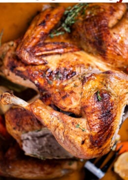 Pinterest pin with a roasting pan with a golden brown spatchcocked turkey resting on top of lemon and vegetables, with melted butter and fresh thyme on the bottom of the pan, and a turkey leg being lifted up by a spatula.