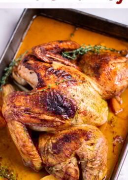 Pinterest pin with a roasting pan with a golden brown spatchcocked turkey resting on top of lemon and vegetables, with melted butter and fresh thyme on the bottom of the pan, and a kitchen towel on the table next to the roasting pan.