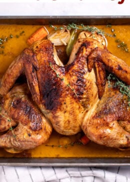 Pinterest pin with a roasting pan with a golden brown spatchcocked turkey resting on top of lemon and vegetables, with melted butter and fresh thyme on the bottom of the pan, and a kitchen towel on the table next to the roasting pan.