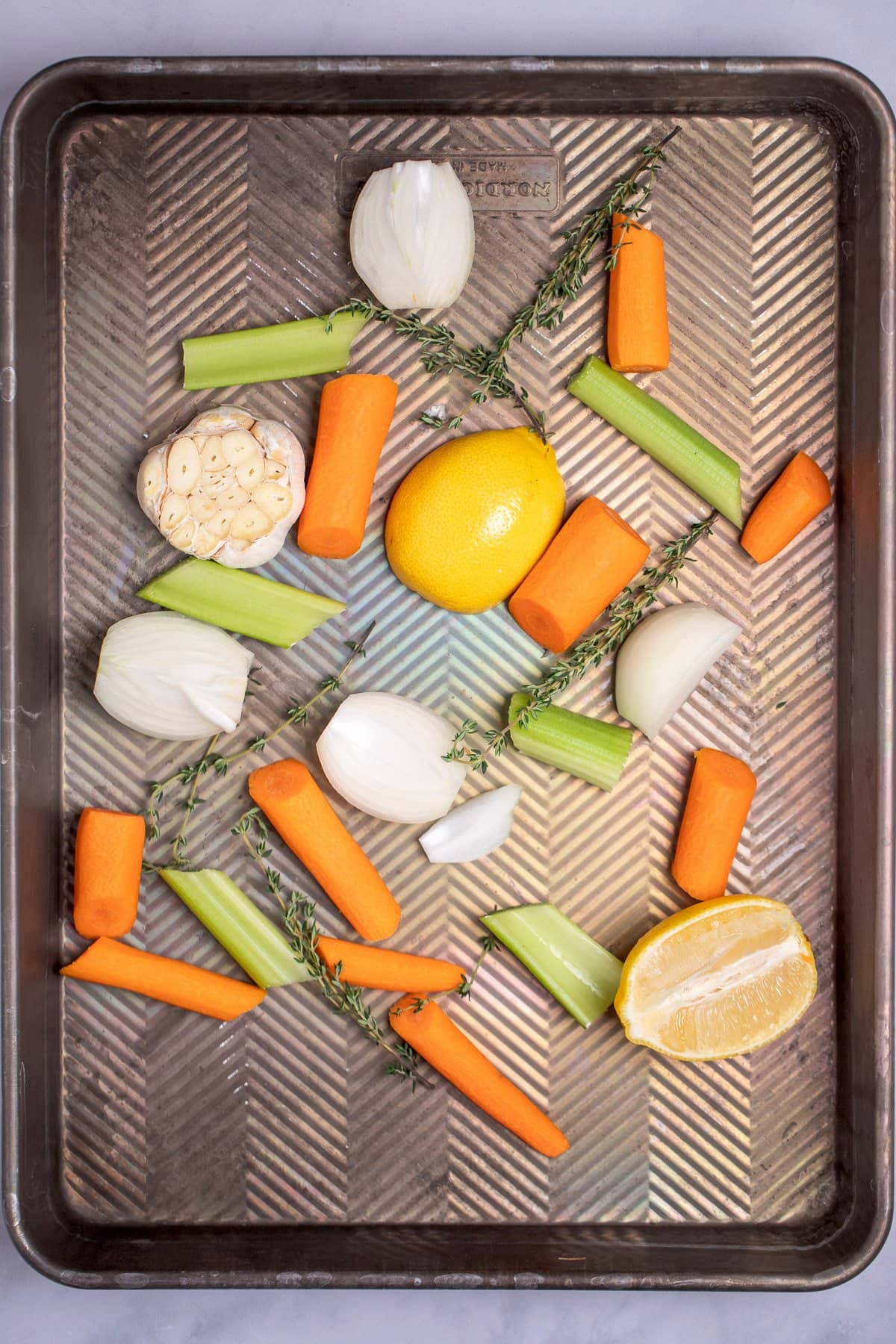A roasting pan with carrots, celery, lemon, garlic, onion, and fresh thyme before being cooked.