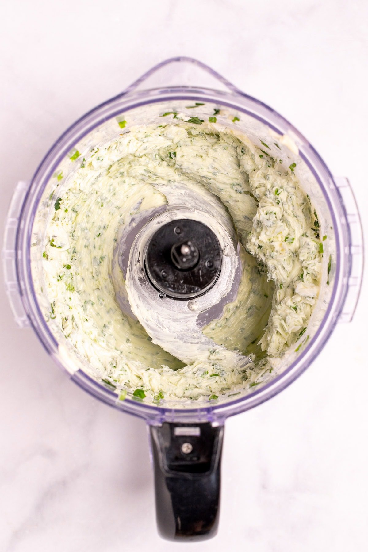 A food processor with whipped butter and fresh herbs.