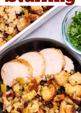 A bowl with gluten free stuffing and turkey slices on a table, in front of a baking dish of stuffing, and next to a small glass bowl of chopped fresh parsley.