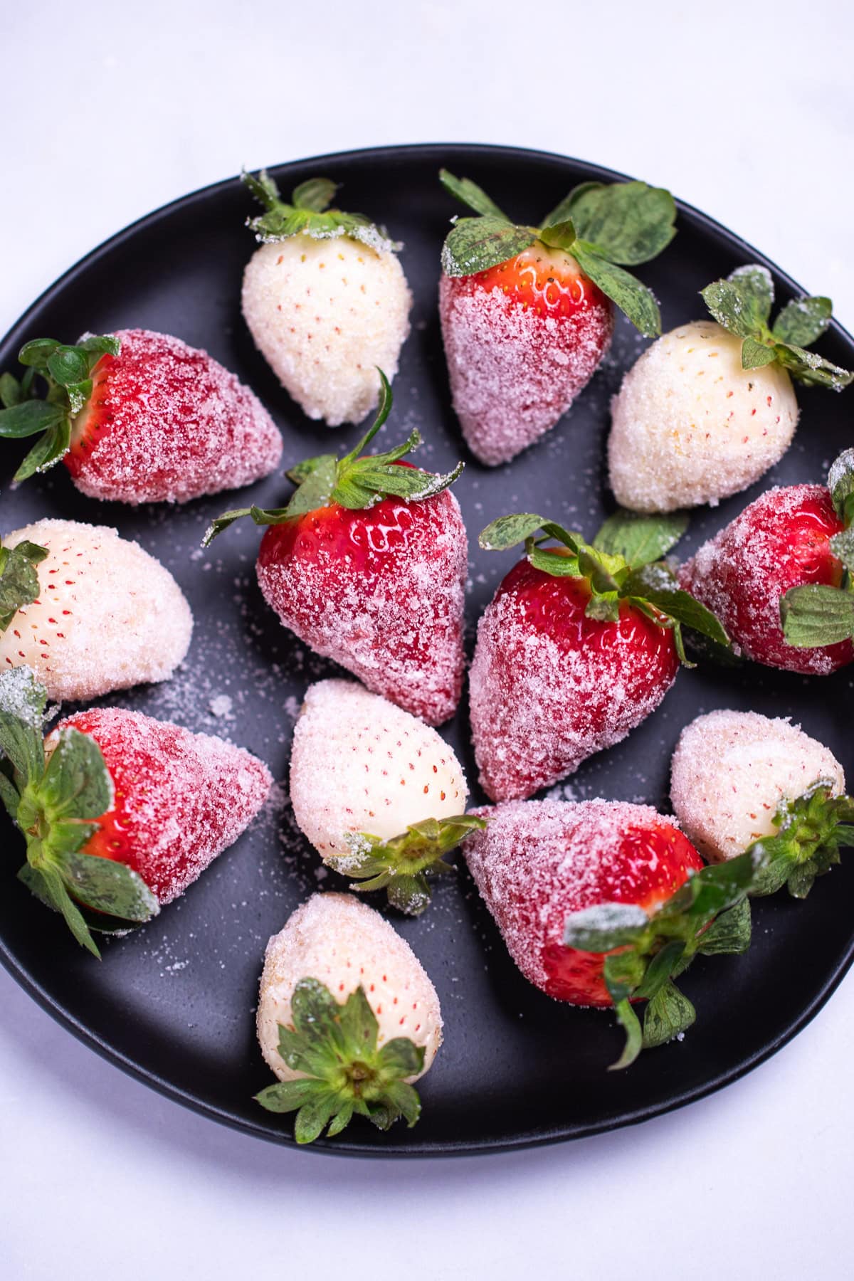 Red and white sugar coated champagne strawberries on a plate.
