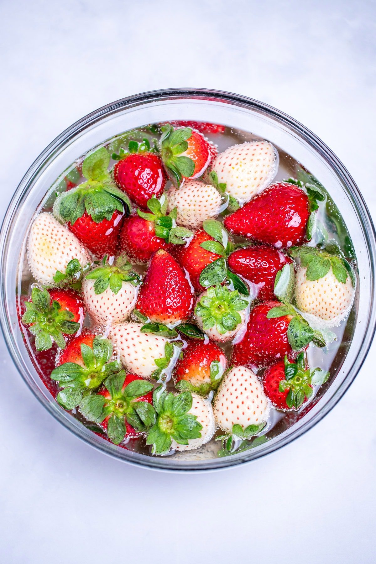 Red and white strawberries soaking in a bowl of champagne.
