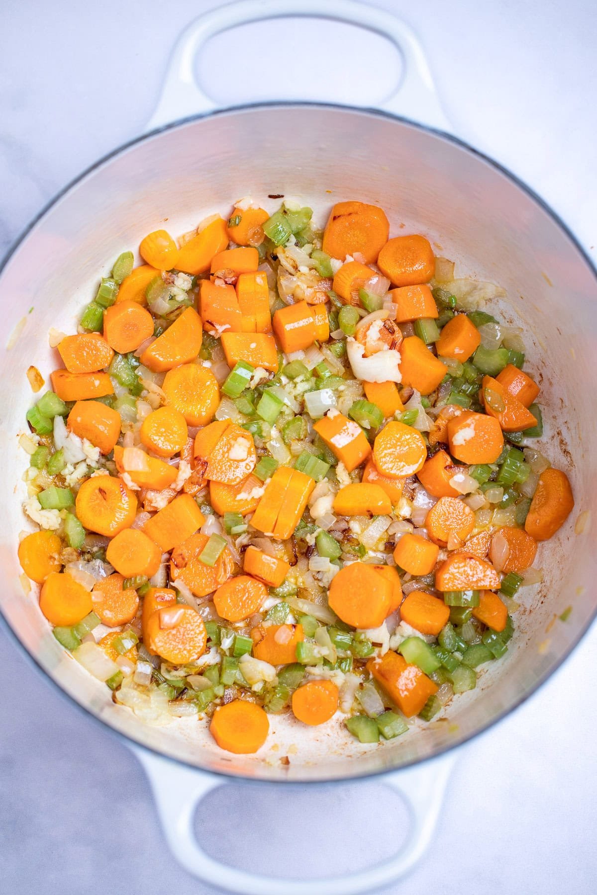 A dutch oven with sautéed onion, celery, and carrots.