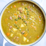 A dutch oven with split pea soup with ham, carrots, and potatoes, with thyme on top.
