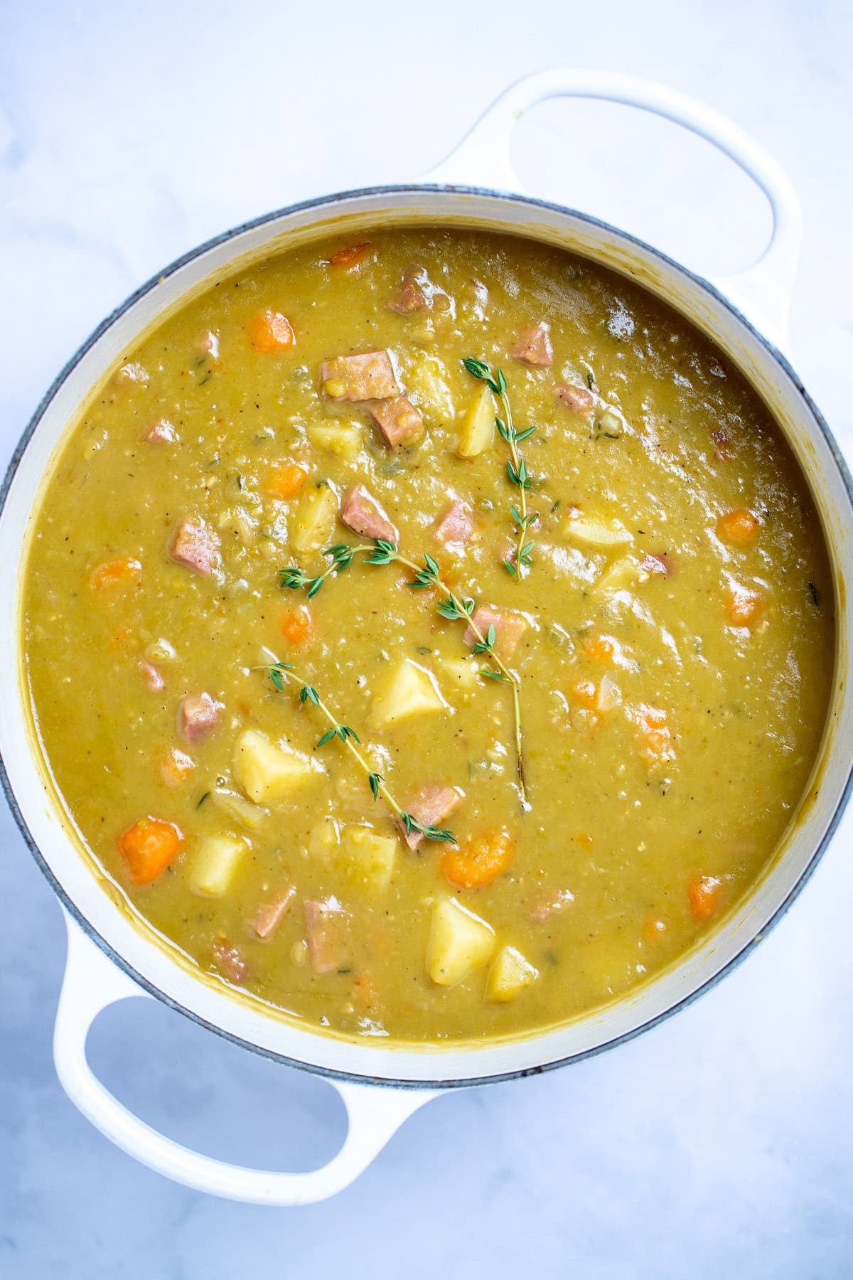 A dutch oven with split pea soup with ham, carrots, and potatoes, with thyme on top.