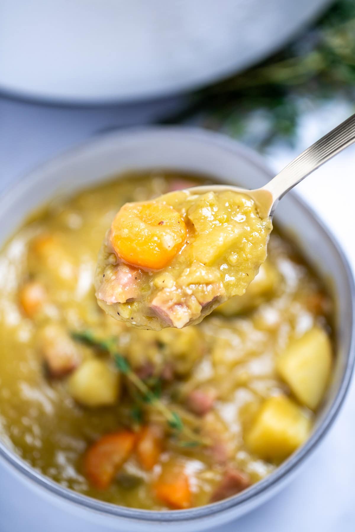 A spoon lifting up split pea soup from a bowl with ham, carrots, celery, and potatoes.