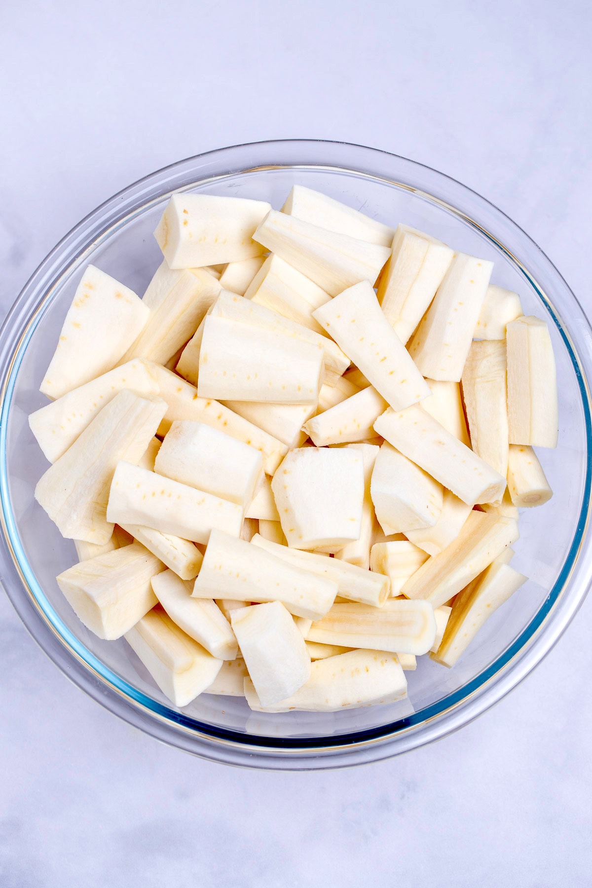 A glass bowl with chopped parsnip pieces on a table.