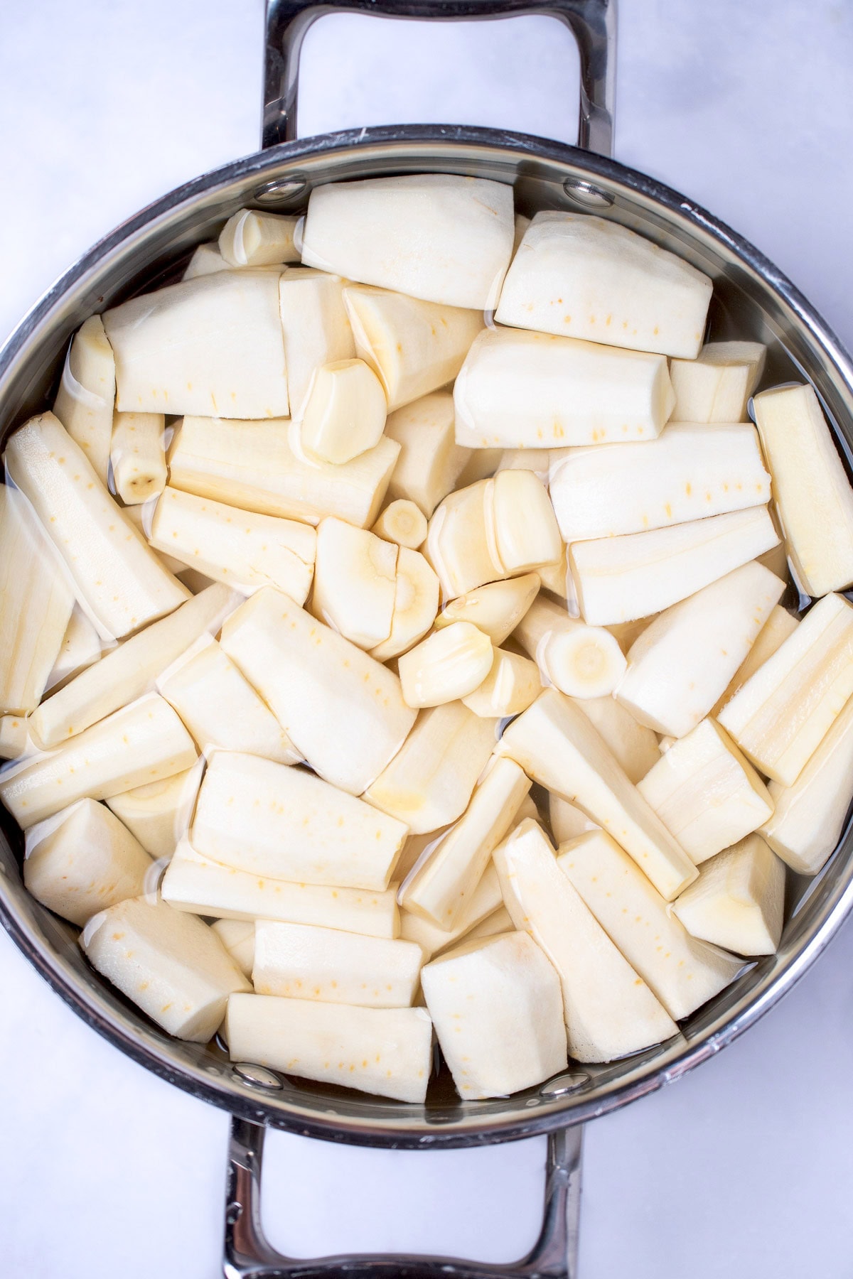 A pot with parsnip pieces, garlic cloves, and water before boiling.