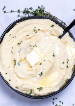 A bowl of parsnip puree topped with butter and thyme, next to fresh thyme on a table.