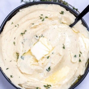 A bowl of parsnip puree topped with butter and thyme, next to fresh thyme on a table.