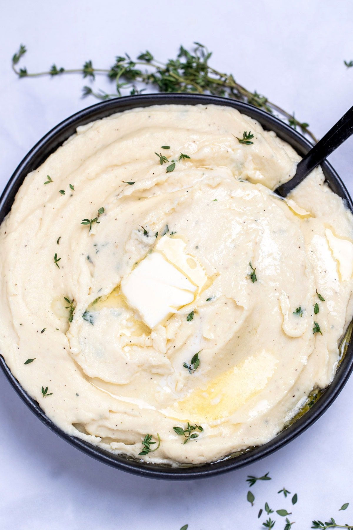 A bowl of parsnip puree topped with butter and thyme, next to fresh thyme on a table.