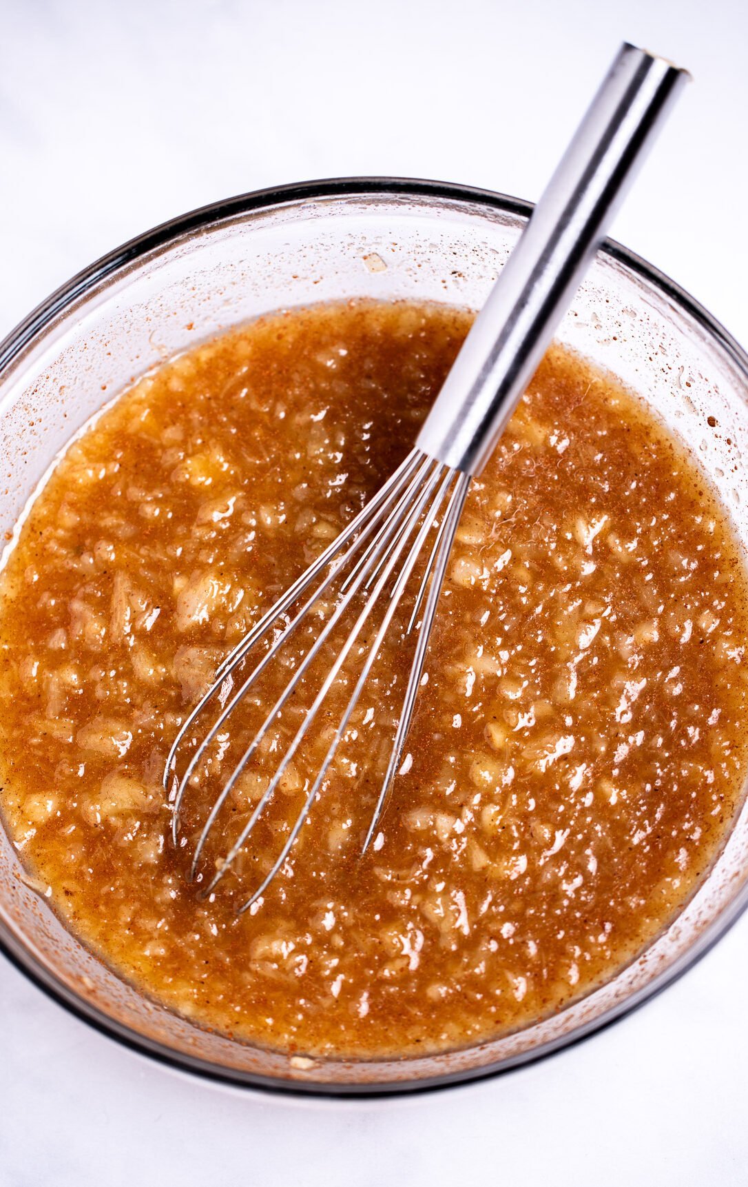 A glass bowl on a table with a whisk, with a pineapple glaze.