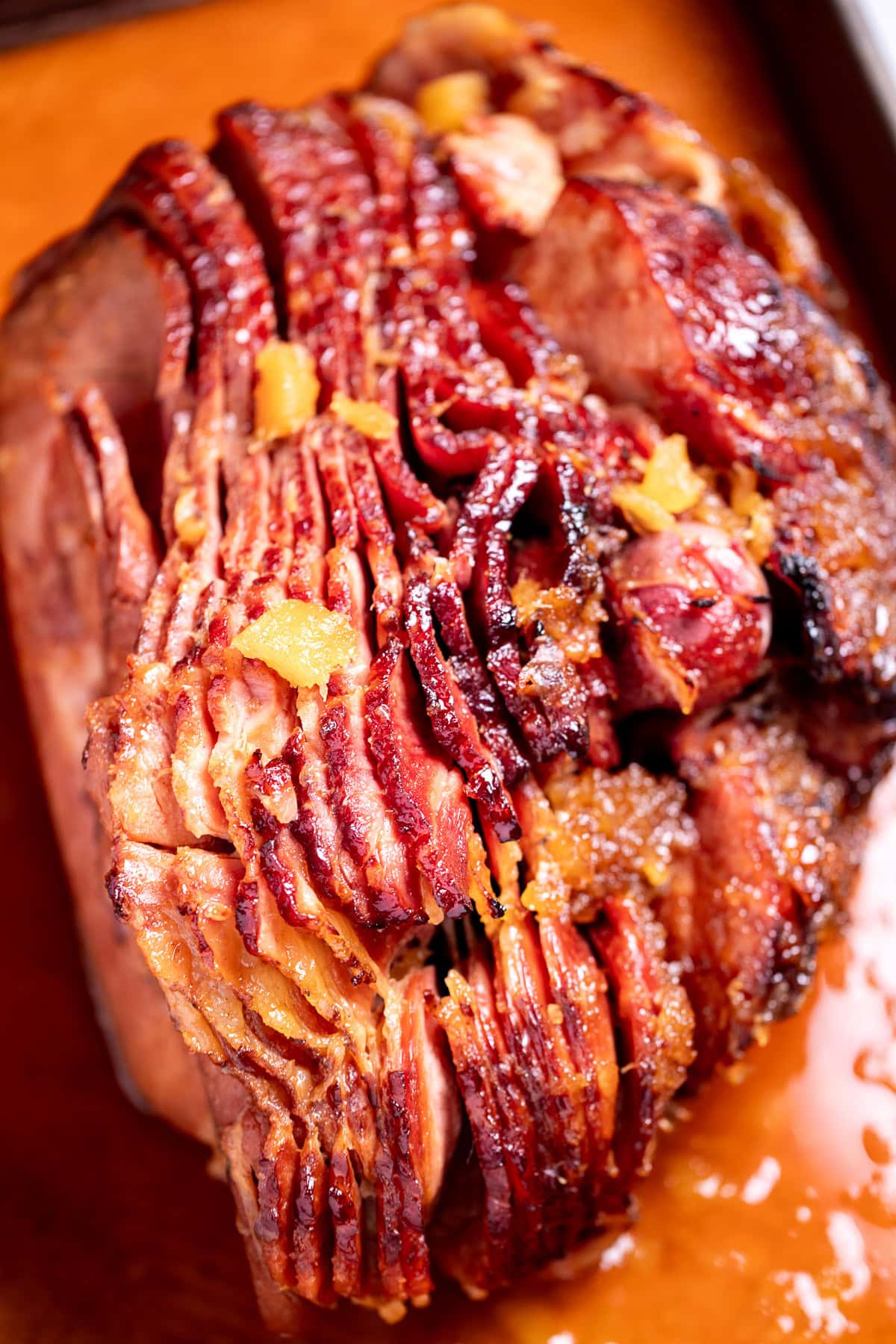 A spiral ham with a pineapple glaze with a caramelized top on a roasting pan with juices.
