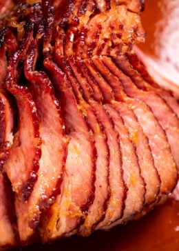 A spiral ham with a pineapple glaze with a caramelized top on a roasting pan with juices.