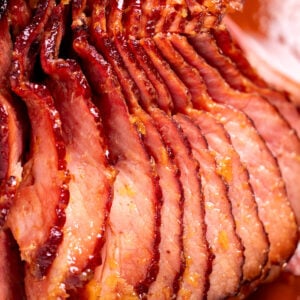 A spiral ham with a pineapple glaze with a caramelized top on a roasting pan with juices.