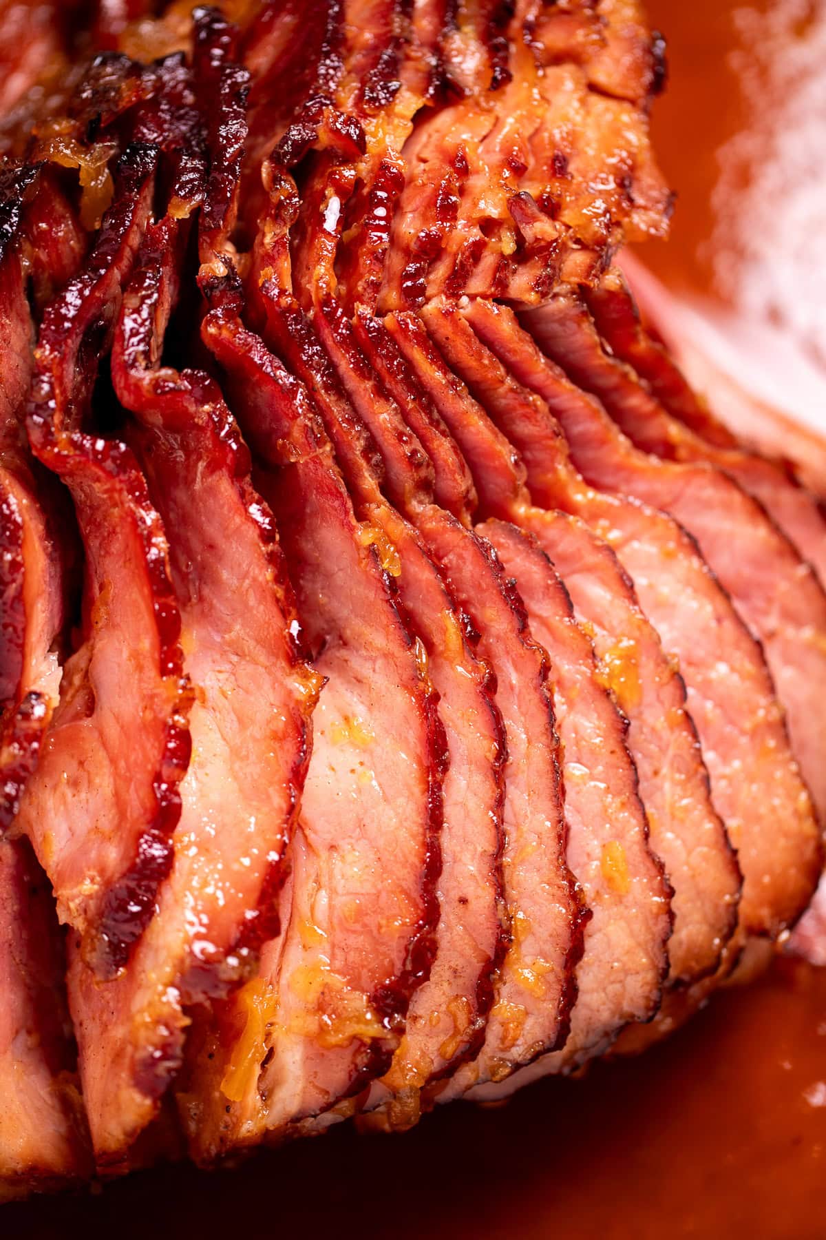 A spiral ham with a pineapple glaze with a caramelized top on a roasting pan with juices.