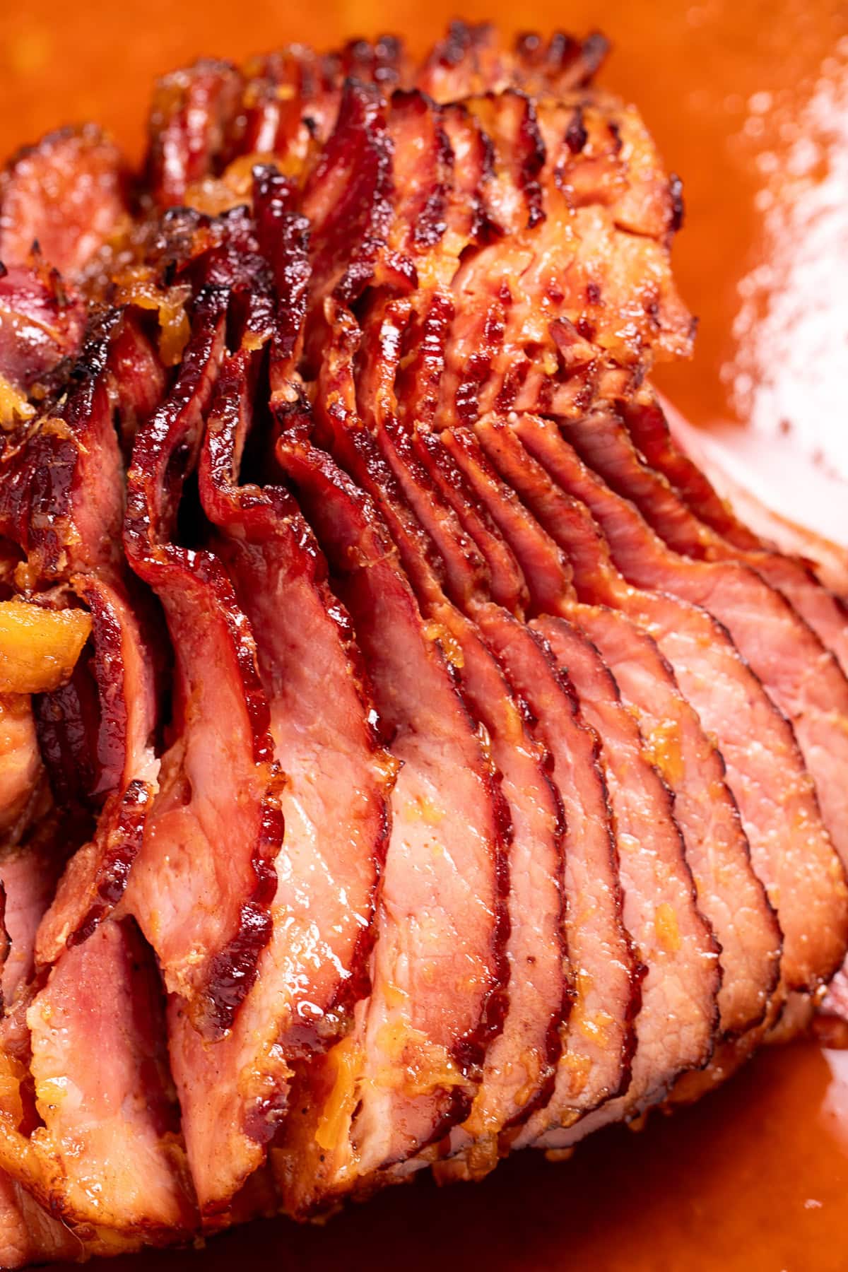 A spiral ham with a pineapple glaze with a caramelized top on a roasting pan with juices.