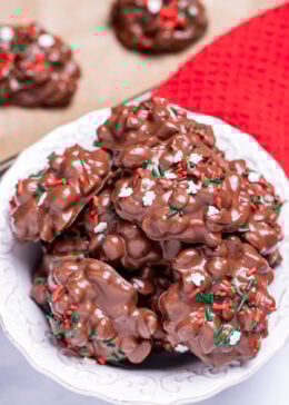 A bowl on a table filled with chocolate peanut clusters topped with sprinkles.