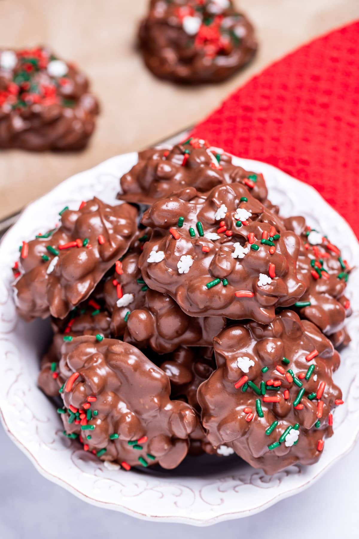 A bowl on a table filled with chocolate peanut clusters topped with sprinkles.