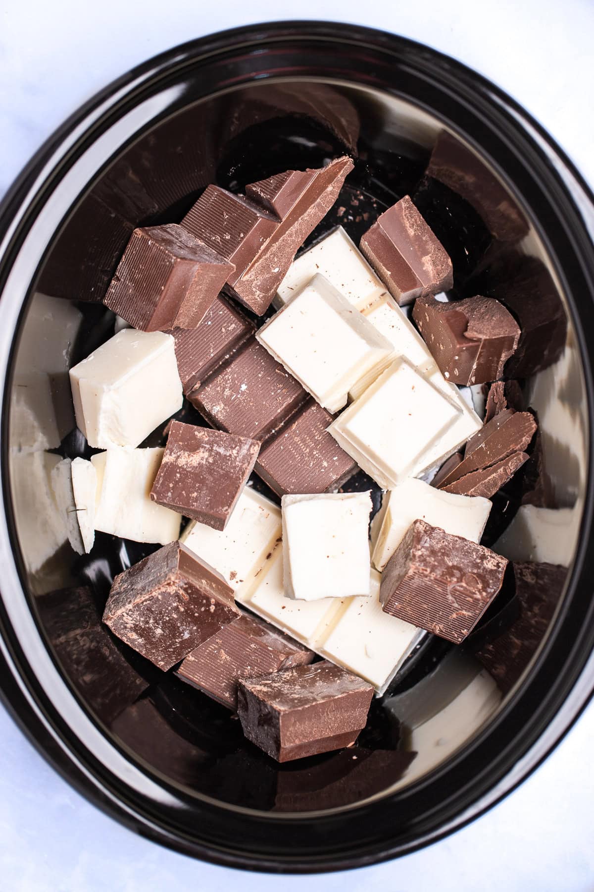 A slow cooker with chocolate and vanilla almond bark in it before cooking.