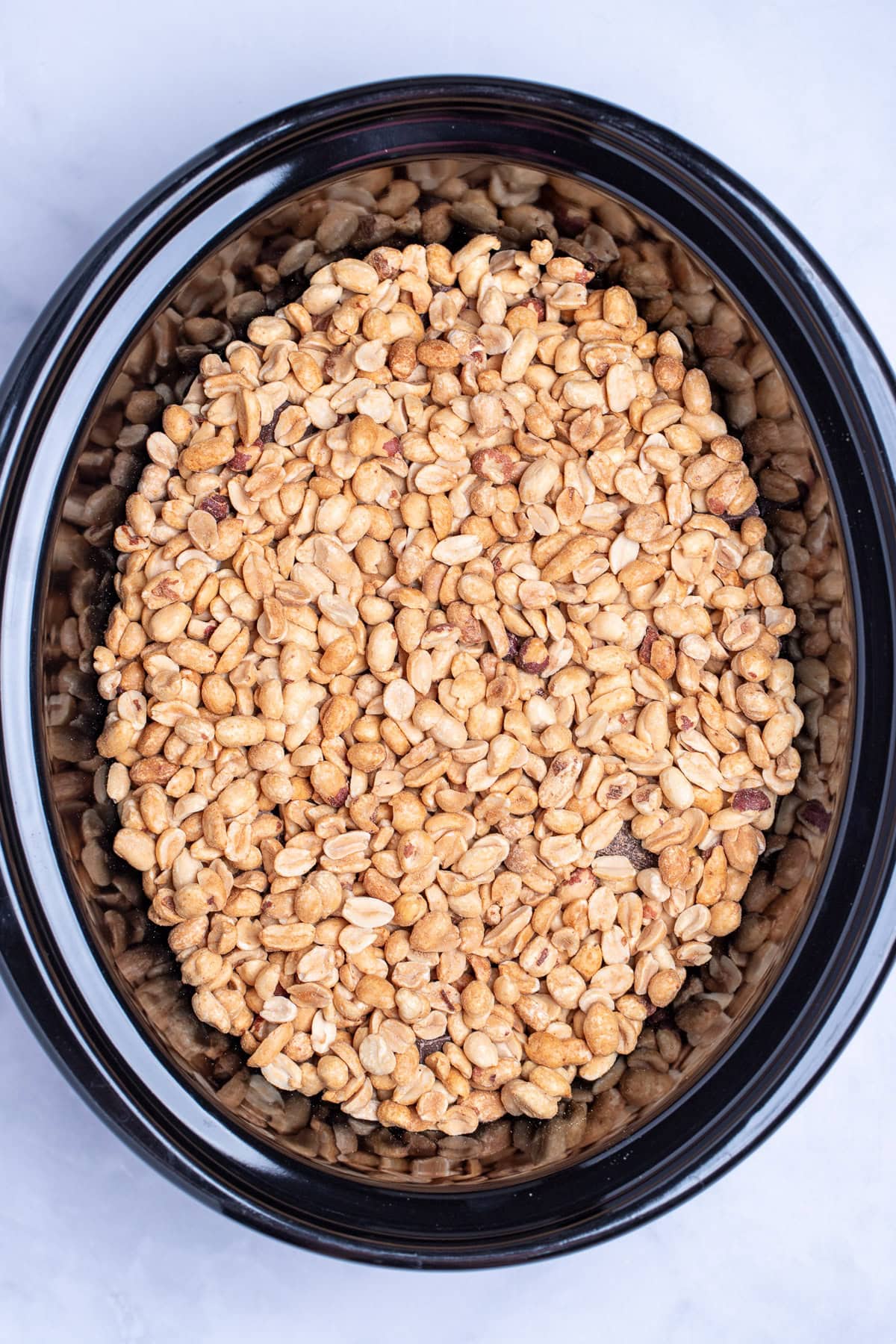 A slow cooker with roasted peanuts on top of almond bark before cooking.