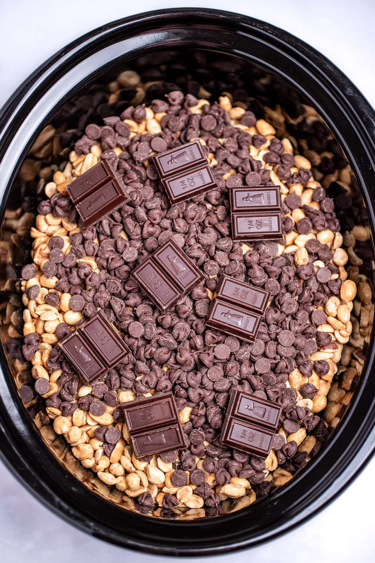 A slow cooker with roasted peanuts topped with chocolate chips and German's chocolate before cooking.