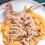 A plate with shredded pork shoulder over sauerkraut with a fork resting on a plate, in front of a slow cooker.