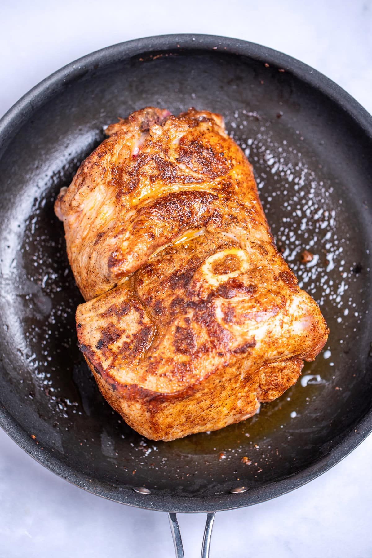A saute pan with a seared bone-in pork shoulder.