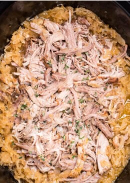 Pinterest pin with a slow cooker with cooked shredded bone-in pork shoulder surrounded by sauerkraut and juices.