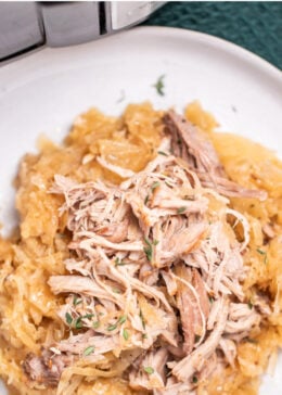 Pinterest pin with a plate with shredded pork shoulder over sauerkraut, in front of a slow cooker.