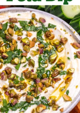 Pinterest pin with a bowl of whipped feta dip topped with chopped parsley, pistachios, olive oil, and honey on a wooden cutting board.