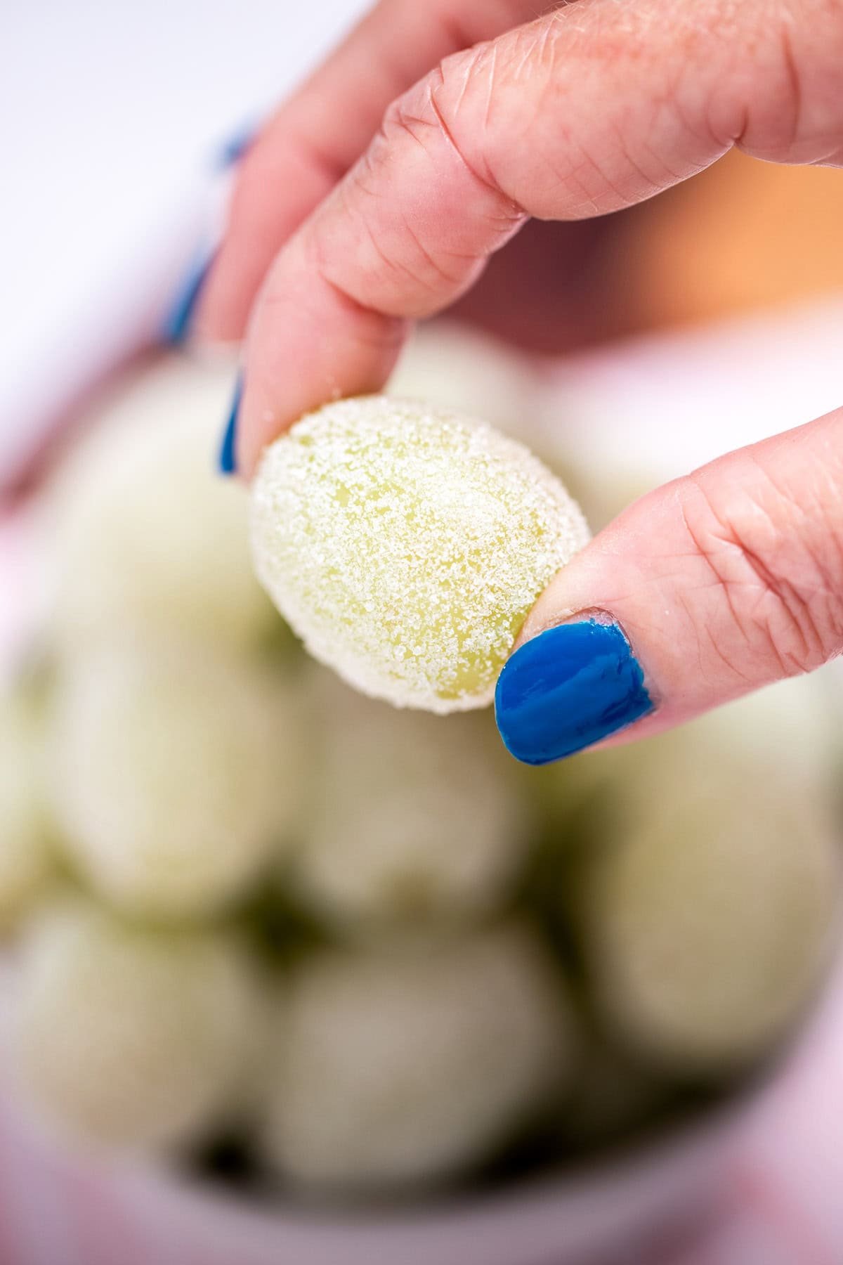 A hand holding a sugared grape over a bowl of grapes.