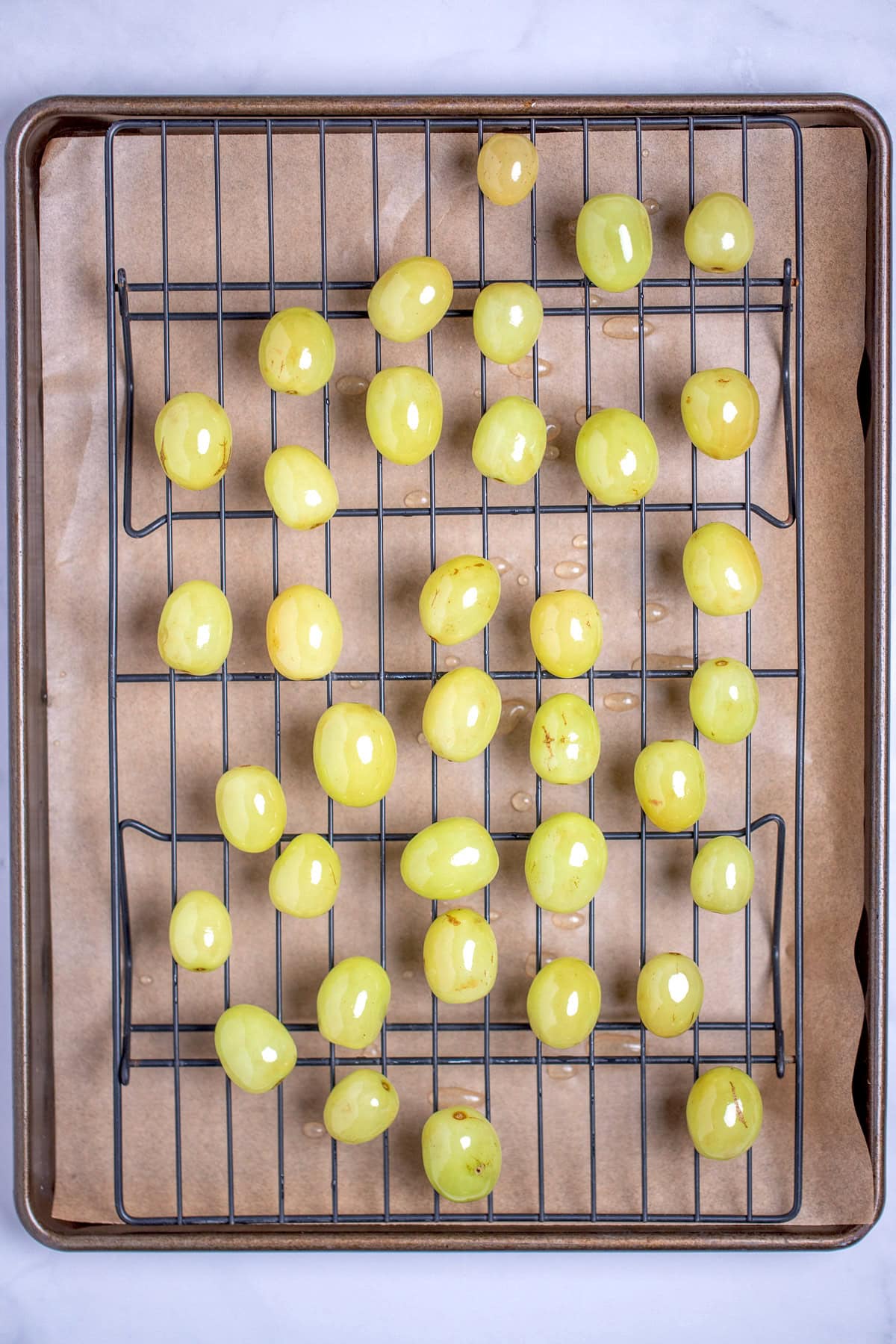 A sheet pan lined with parchment paper and a rack with grapes in sugar syrup drying.