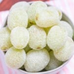 A bowl of sugared grapes on a tea towel on a wooden cutting board.